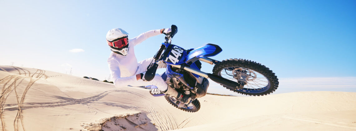 Sand, motor sports and man in air with motorbike for adrenaline, adventure and freedom in desert. Action, extreme sport and male person on bike on dunes for training, exercise and race or challenge