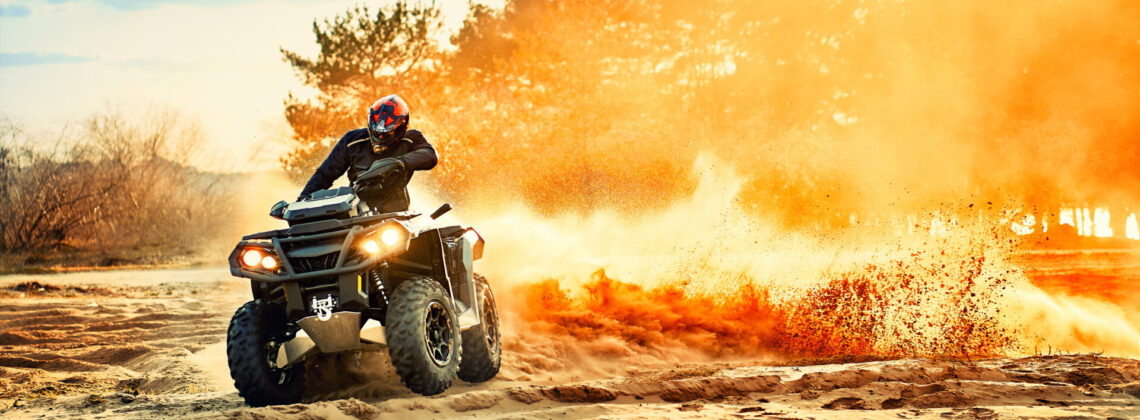 Teen riding ATV in sand dunes making a turn in the sand