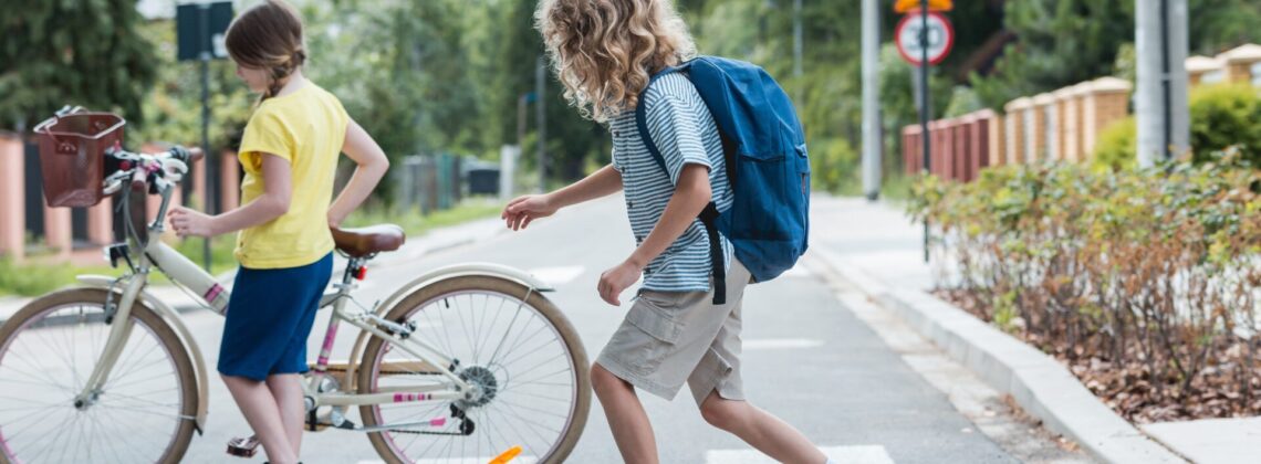 Boy on a skateboard and a girl with a bicycle cross the street