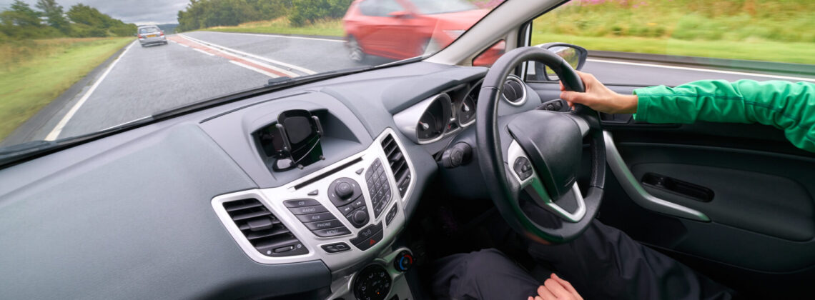 The interior of a car of a female driver driving along a busy road in poor weather with traffic passing in the opposite direction on an English single carriageway.