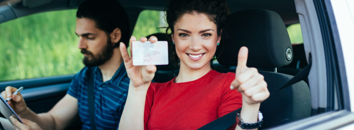 Driving school. Beautiful young woman successfully passed driving school test. She looking sitting in car, looking at camera and holding driving license in hand.