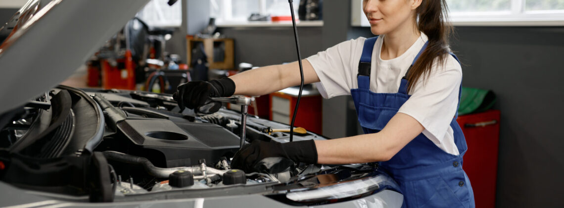 Young satisfied female mechanic fixing engine at service car garage