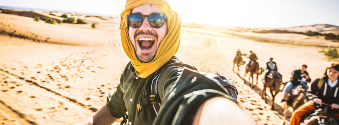 Happy tourist having fun enjoying group camel ride tour in the desert – Travel, vacation activities and adventure concept