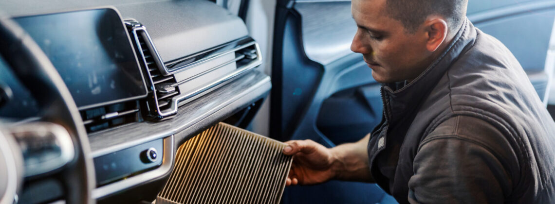 A worker taking out old air filter in car at mechanic’s shop.