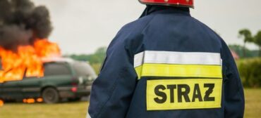 Strażak gasi płonący samochód, który podlega ubezpieczeniu od pożaru.